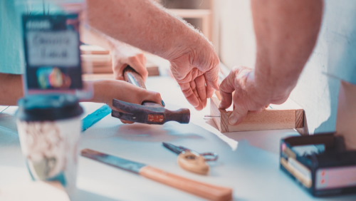 Person holding a black hand tool and doing woodwork